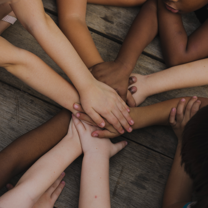 Children with diverse skin tones laying in a circle stacking hands