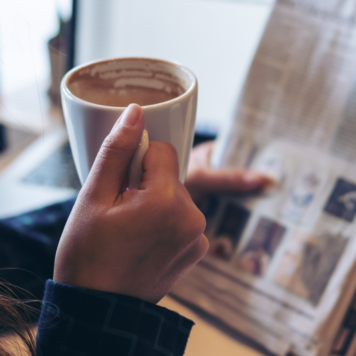 Person relaxing and reading newspaper with cup of coffee in hand