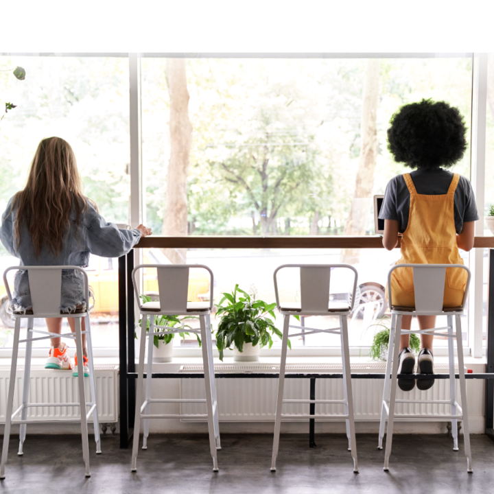 Two people sitting at opposite ends of a high-top table facing a window